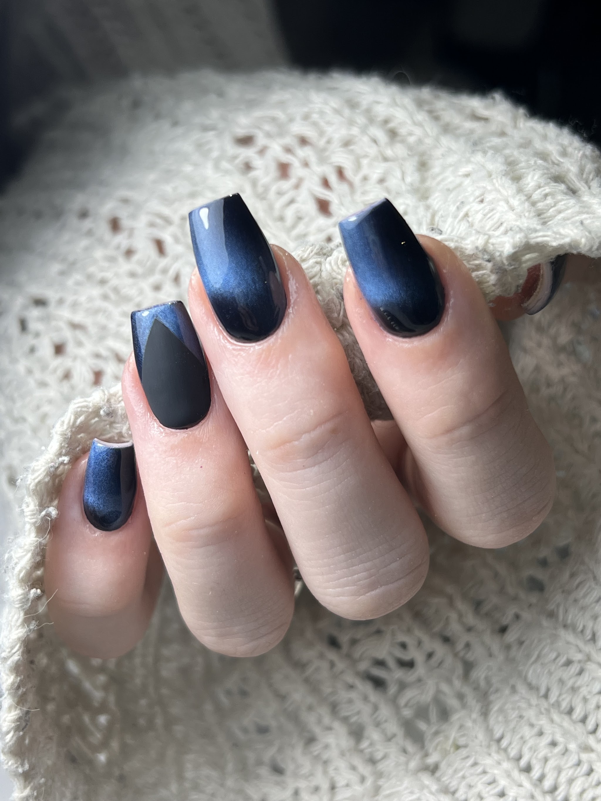 Donkerblauwe cat-eye nagels bij een witte gebreide trui